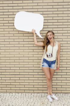 Beautiful and young teenager holding a thought balloon, in front of a brick wall