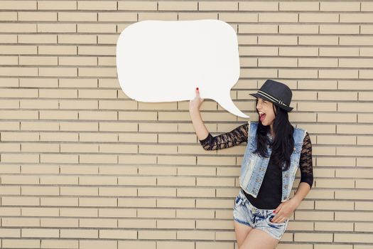 Beautiful and young teenager holding a thought balloon, in front of a brick wall