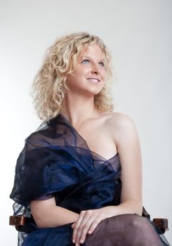 young woman in evening dress sitting in the chair smiling - isolated on light gray