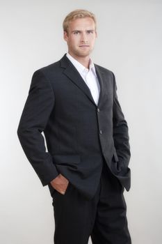 portrait of a young businessman with blond hair in suit standing - isolated on light gray