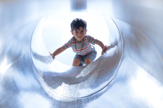 Toddler boy playing in playgroung tunnel under bright sky