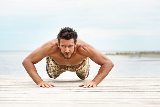 Fit shirtless male fitness model in push up exercise outdoors.