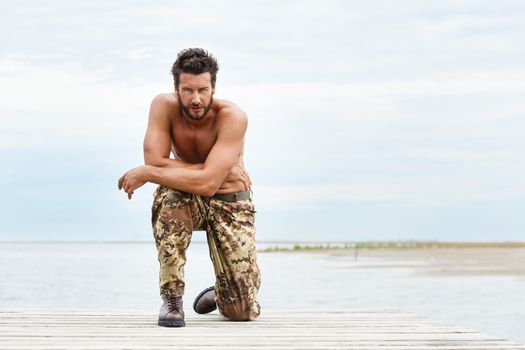Portrait of a handsome muscular man in camouflage trousers with cloudy sky background 