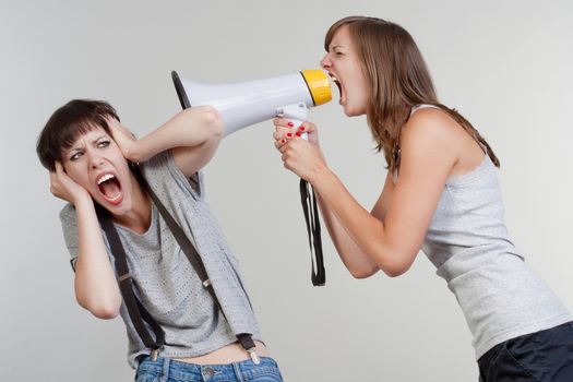 angry woman yelling into a megaphone to another scared girl - isolated on gray