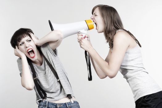 angry woman yelling into a megaphone to another scared girl - isolated on gray