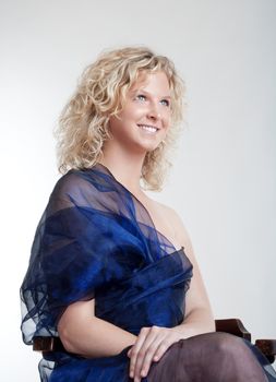 young woman in evening dress sitting in the chair smiling - isolated on light gray