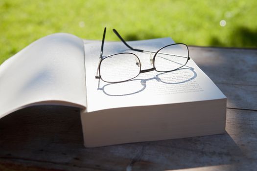 closeup of glasses and an opened book on a table in the garden