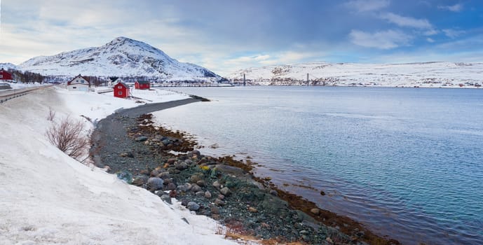 Winter in Norway - mountains with red house and the ocean. Panorama