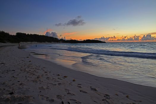 A sweeping beach, with the waves lapping the shore, as the sun rises on the horizon