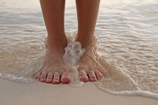 Two feet, on the sand as the surf washes over them. Warm filter applied