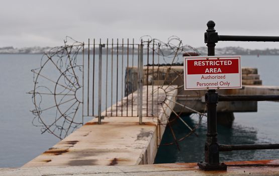 A restricted area sign, in front of a locked gate surrounded by barbed wire