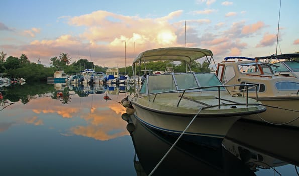 Boats moored in a natural harbour, with clouds refelcted in the smooth, calm water