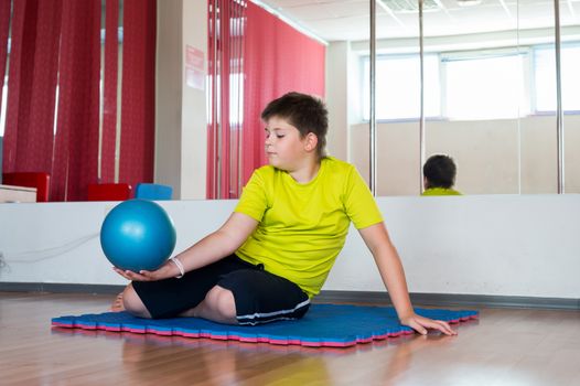 Boy does exercise with the ball in the gym