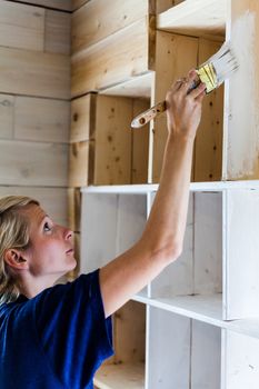 Real Home Renovation (not studio) - Woman Applying White Paint on a Wood Library.