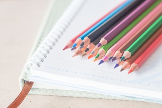 Closeup colorful pencil crayons on spiral notebook and green notebook, stock photo