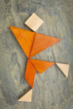 abstract of a dancing, running or walking figure built from seven tangram wooden pieces, a traditional Chinese puzzle game; slate rock background background, the artwork copyright by the photographer