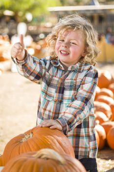 Adorable Little Boy Leaning on Pumpkin Gives a Thumbs Up in a Rustic Ranch Setting at the Pumpkin Patch.