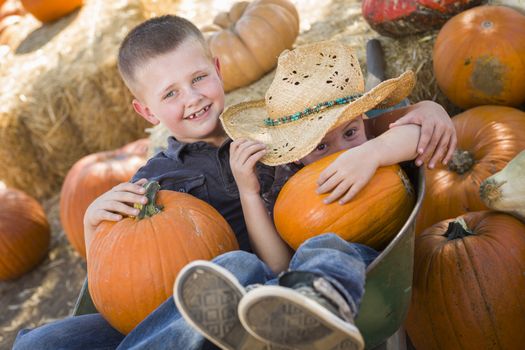 Two Little Boys Playing in Wheelbarrow at the Pumpkin Patch in a Rustic Country Setting.