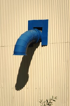 A blue pipe outlet on the side of a cream colored, corrugated metal sheeting wall.