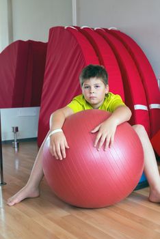 Boy does exercise with the ball in the gym