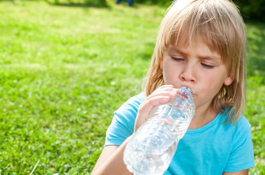 Cute little girl drinking water in a summer garden