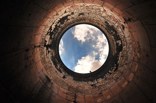 A view upwards inside a large empty tank, with blue sky and clouds visible through the opening.