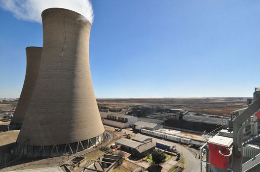 Two concrete cooling towers on the left with a view of the horizon and rural landscape. One tower with cloud of steam rising.