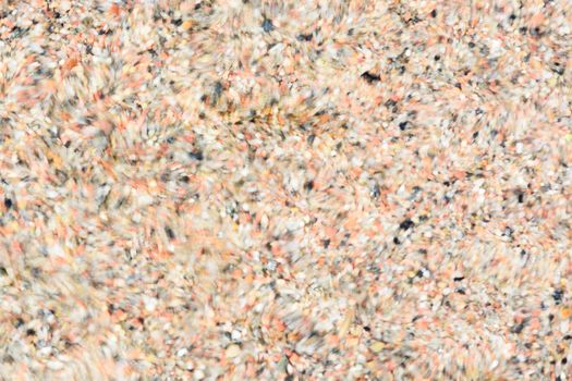 Abstract background blur - closeup of water moving over small pebbles in shallow water creating many circular patterns.