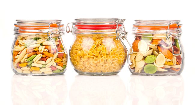 the various raw pasta in a glass jar, isolated on white background