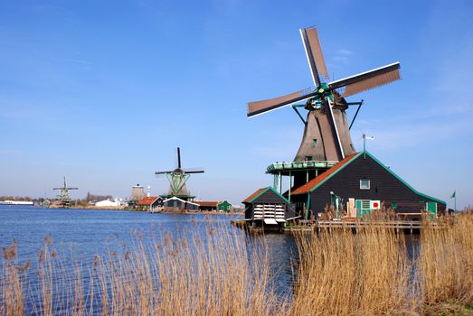 Photo shows Dutch windmills, houses and lake.