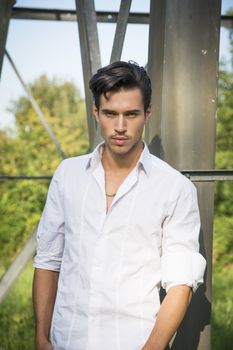 Handsome young man leaning against metal electricity trellis, looking at camera