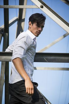 Handsome young man hanging from metal electricity trellis, looking at camera