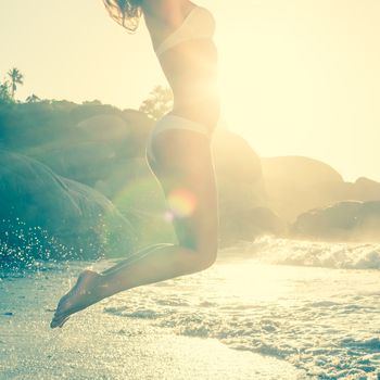 Beautiful jumping blonde in white bikini at the beach on a sunny day