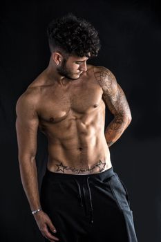 Young athletic man with tattoo posing isolated over black background, studio shot