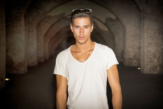 Handsome young man in old building walking inside gallery, looking at camera