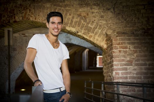 Handsome young man in old building leaning on handrail, smiling and looking at camera