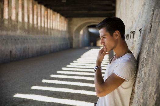 Handsome young man in old building against brick wall, looking down