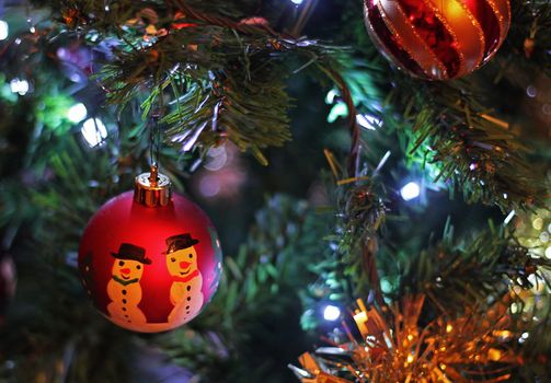Two Christmas baubles, in color, hanging on a green tree with tinsle