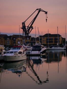 A dockside crane and boats, silhouetted against the setting sun