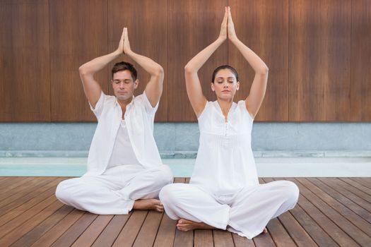Attractive couple in white sitting in lotus pose with hands together in health spa
