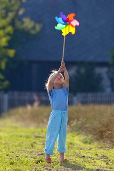boy with long blond hair playing with pinwheel outside