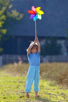 boy with long blond hair playing with pinwheel outside