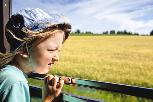 boy with long blond hair and hat looking out the train window