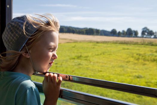 boy with long blond hair and hat looking out the train window