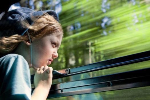 boy with long blond hair and hat looking out the train window