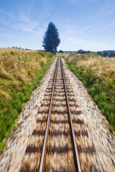 View of narrow gauge railroad track from rear window of train riding through landscape