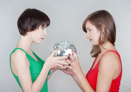 two female teenage friends holding a disco ball looking - isolated on gray