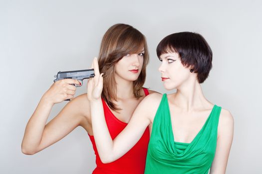 two young female friends playing with a gun - isolated on gray