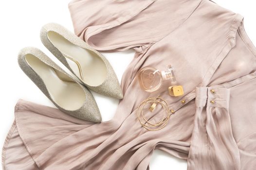 Outfit of stylish ladies clothing on a white background with elegant silver court shoes, gold bangles and a perfume bottle on a neutral tone dress or tunic for smart casual wear or evening wear