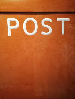 Rusty orange mailbox with Post written on it.